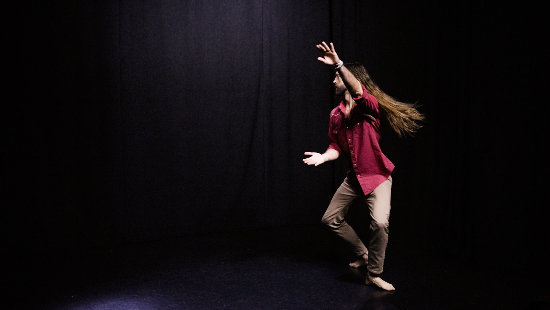 quantum healing practitioner Cabe Lindsay dances with long hair flying in a spacious black studio