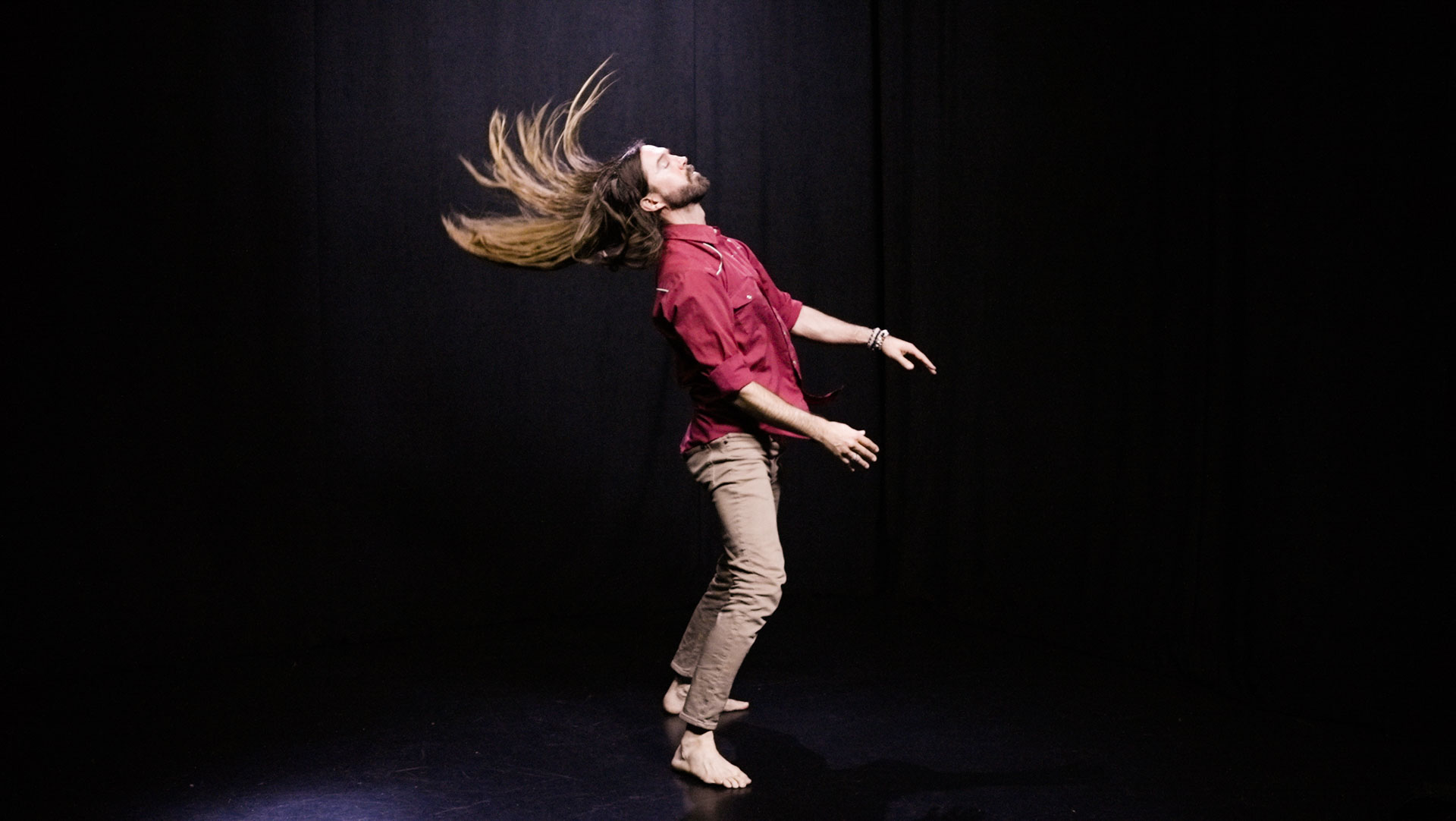 quantum healing practitioner Cabe Lindsay dances with long hair flying in a spacious black studio