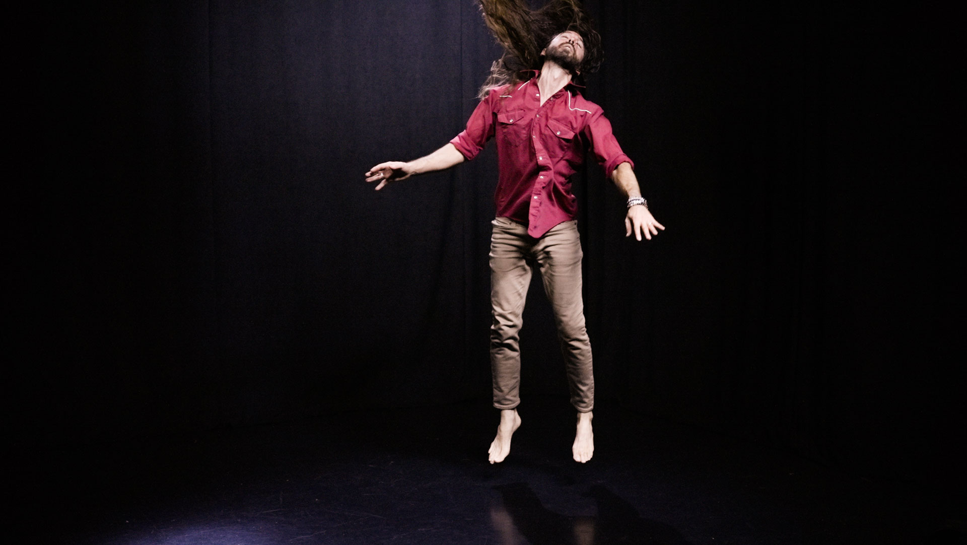 quantum healing practitioner Cabe Lindsay dances with long hair flying in a spacious black studio