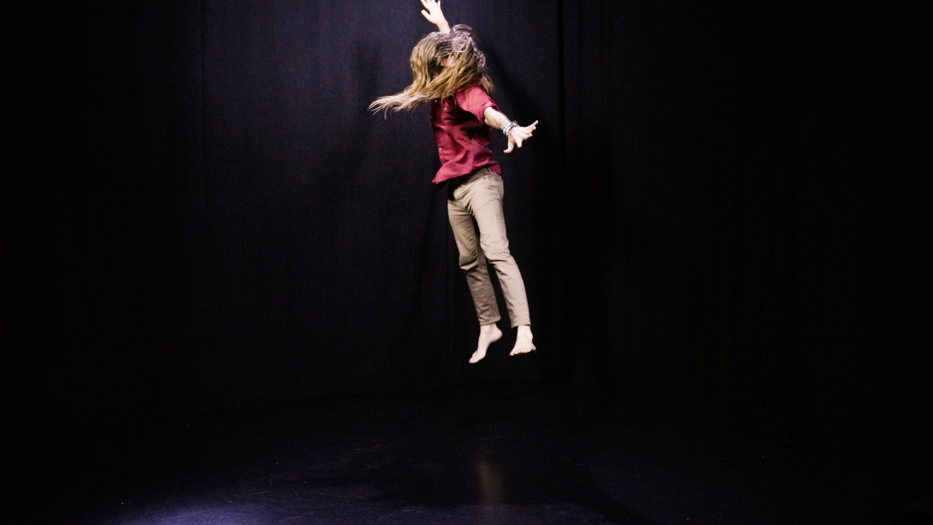 quantum healing practitioner Cabe Lindsay dances with long hair flying in a spacious black studio