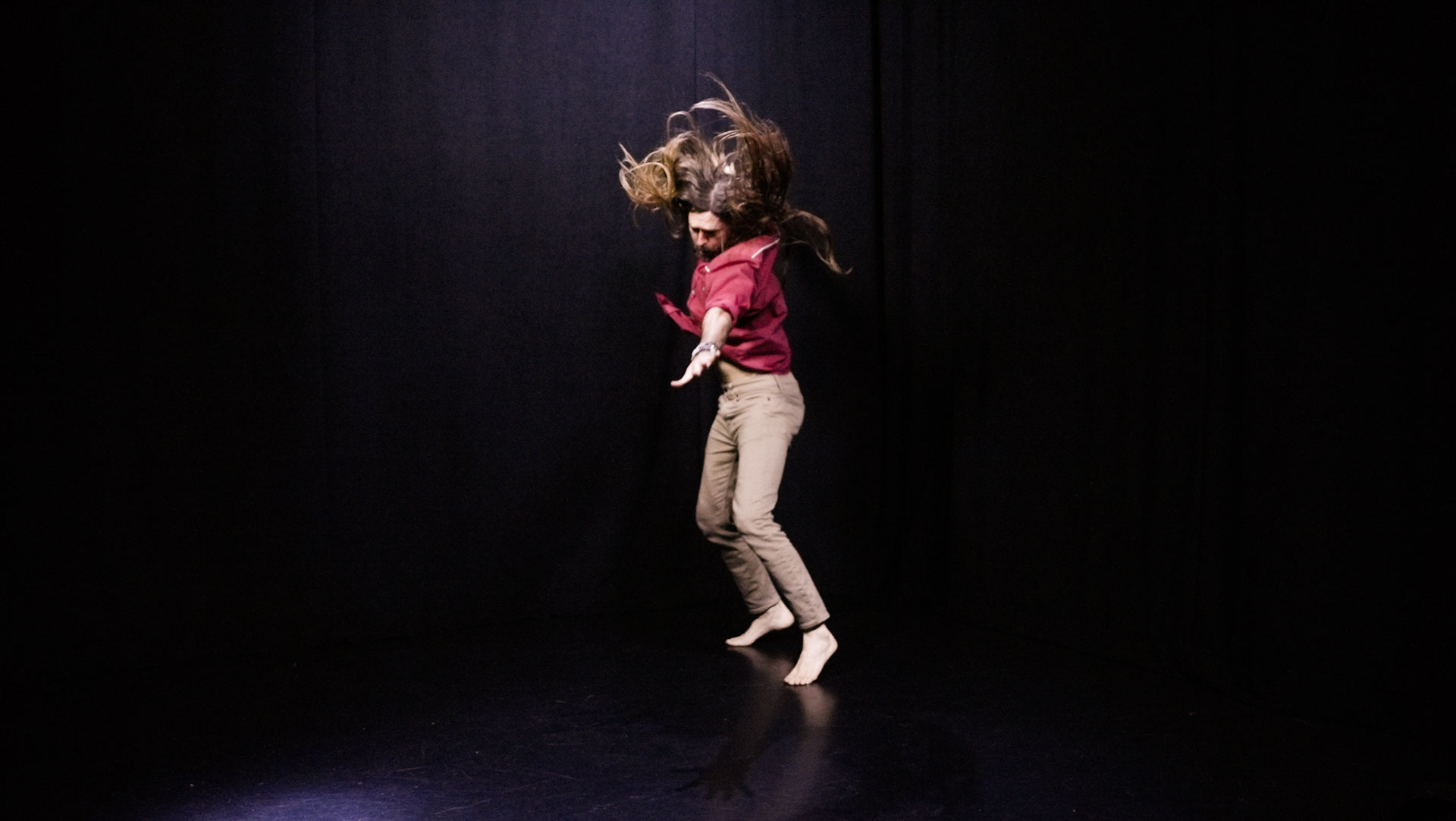 quantum healing practitioner Cabe Lindsay dances with long hair flying in a spacious black studio