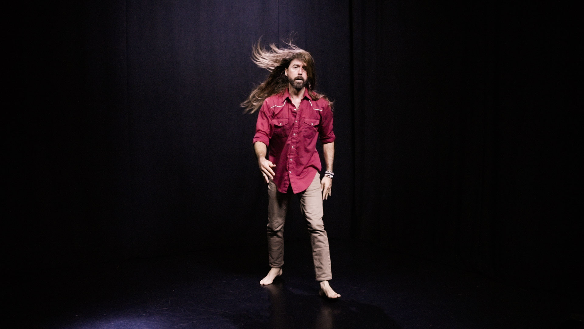 quantum healing practitioner Cabe Lindsay dances with long hair flying in a spacious black studio
